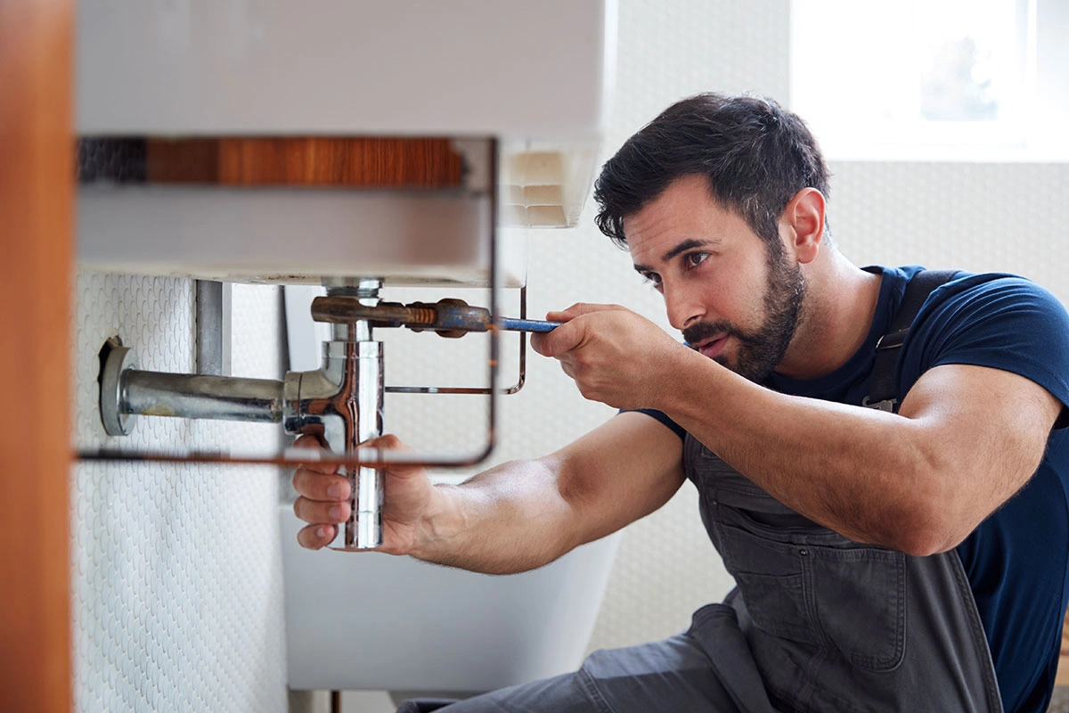 Plumber in blue uniform repairing sink pipes in a bathroom.